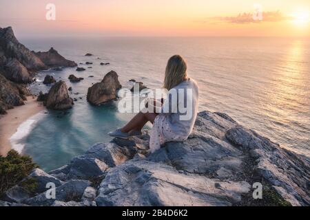 Schöne Touristenfrauen, die den Sonnenuntergang am Strand Praia da Ursa genießen. Surreale Landschaft von Sintra, Portugal. Küstenlandschaft am Atlantik. Stockfoto