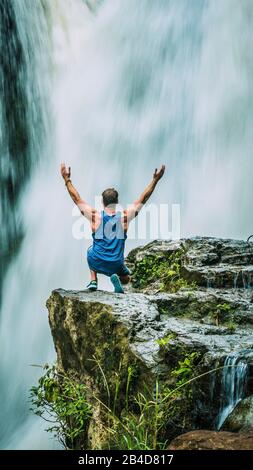 Mann, der vor dem Tegenungan-Wasserfall in der Nähe von Ubud sitzt, hebt die Hände und hapsodize es, Bali, Indonesien. Stockfoto