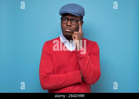 Ernster verwirrter afrikanischer Mann, der sein Kinn berührt, nachdenklich und skeptisch über etwas aussieht, tief in Gedanken, zögert, Entscheidung zu treffen, frowni Stockfoto