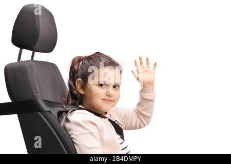 Mädchen auf einem Autositz mit einem Sicherheitsgurt, der auf die Kamera blickt und auf weißem Hintergrund winkt Stockfoto