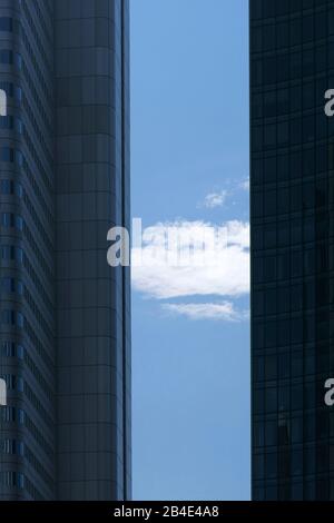 Eine Wolke und den blauen Himmel zwischen den Ecken und Kanten von zwei modernen Wolkenkratzern. Stockfoto