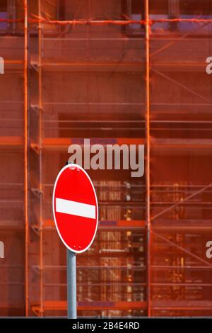 Die Nahaufnahme eines Gerüsts mit Strebepfeilern und Sicherheitsnetze, vor dem steht ein rotes Einbahnstraße unterzeichnen. Stockfoto