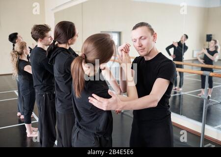 Der junge Lehrer des modernen Balletttanzens wird von einem seiner Schüler gestellt und hilft ihr beim Training Stockfoto