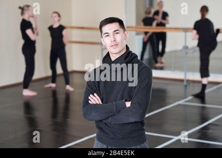 Junger, selbstbewusster Trainer des modernen Balletttanzkurses, der die Arme auf der Brust überquerte, während er im Studio vor der Kamera stand Stockfoto