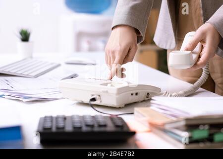 Junge, elegante Büromanagerin oder Geschäftsfrau, die beim Wählen der Nummer die Telefon-Taste drückt, um einen der Kunden anzurufen Stockfoto