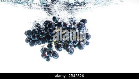 Viele rote Trauben, die auf dem Hintergrund in kristallklares Wasser spritzen Stockfoto
