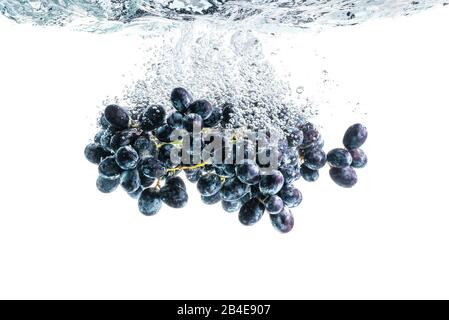 Viele rote Trauben, die auf dem Hintergrund in kristallklares Wasser spritzen Stockfoto