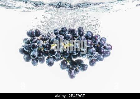 Viele rote Trauben, die auf dem Hintergrund in kristallklares Wasser spritzen Stockfoto