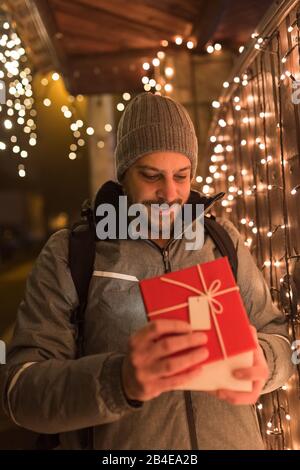 Mann öffnet Geschenkbox im Freien. Weihnachts-Neujahr-Überraschungskonzept. Stockfoto