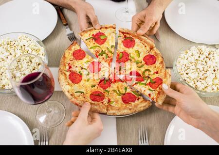 Hände von mehreren jungen Freunden, die beim gemeinsamen Mittagessen im Café oder zu Hause Scheiben der appetitlichen Pizza einnehmen Stockfoto