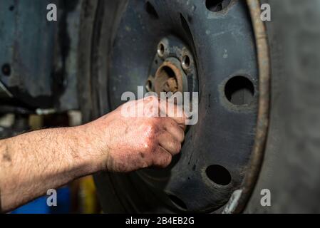 Der Automechaniker fügt die Schrauben ein, mit denen das Stahlrad des Fahrzeugs vor dem Einsatz des Pneumatikschlüssels befestigt ist. Stockfoto