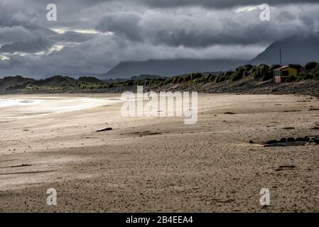 Abendstimmung mit dunklem, bewölktem Himmel am einsamen Strand an Irlands coas, einem einsamen Wandererspaziergang am Strand Stockfoto