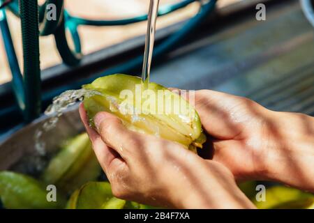 Nahaufnahme der Frau, die frische organische Sternfrucht (Averrhoa carambola), alias Carambola, waschen, unter fließendem Wasser spülen und mit den Fingern scheuern Stockfoto