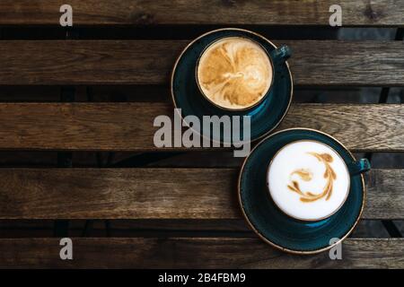 Zwei schöne rosa Tassen Cappuccino mit Latte Art auf dem hölzernen Tisch Stockfoto