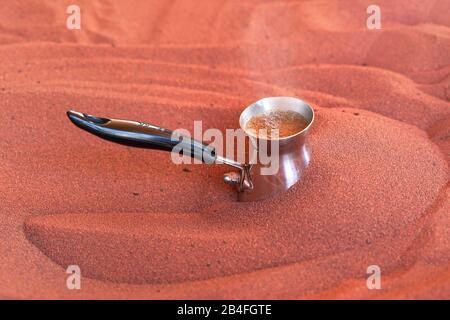 Kaffee auf der Straße auf traditionelle arabische Art zubereitet, ZVe oder Ibrik kleine türkische Kaffeekanne wird in rotem heißem Sand platziert, bis flüssige Brühen, Nahaufnahme deta Stockfoto