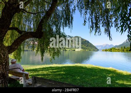 Grundlsee, Grundlsee-Ostende bei Gössl, Blick nach Westen zum Dorf Grundlsee und Berg Zinken, Mann auf Bank im Ausseerland-Salzkammergut, Steiermark, Styria, Österreich Stockfoto