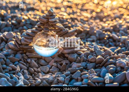 Stapel von pyramidenförmigen Kieselsteinen mit Kristallkugel am Strand von MoÅ¡Ä‡eniÄka Draga bei Sonnenaufgang, Kreis Primorje-Gorski Kotar, Kroatien Stockfoto