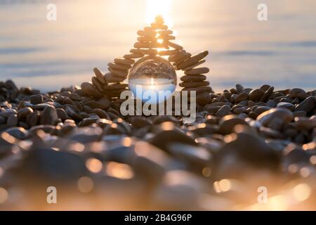 Stapel von pyramidenförmigen Kieselsteinen mit Kristallkugel am Strand von MoÅ¡Ä‡eniÄka Draga bei Sonnenaufgang, Kreis Primorje-Gorski Kotar, Kroatien Stockfoto