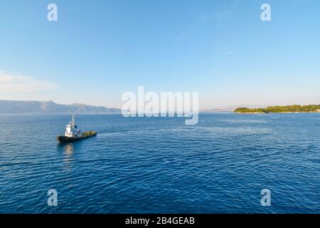 Ein kleines Lotsenboot fährt über die ägeische See zu einem Kreuzfahrtschiff (nicht sichtbar) direkt vor der Insel Korfu, Griechenland. Stockfoto
