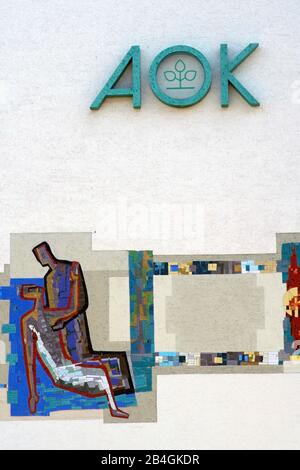 Das Logo der Krankenkasse AOK an der Fassade eines Büro- und Geschäftshauses mit Mosaikgemälde in Alzenau. Stockfoto