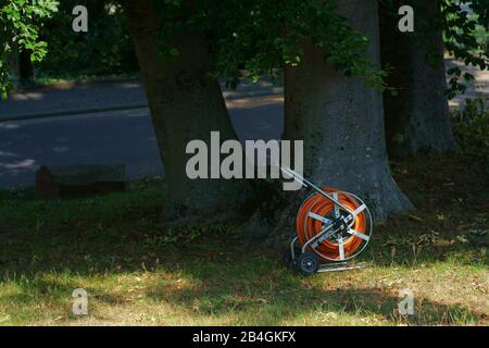 Ein Spiralkabel Gartenschlauch unter einem Baum im Park. Stockfoto