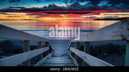 Die Holztreppe, die zum atemberaubenden Sonnenuntergang über dem Horizont führt, während die Nacht fällt Stockfoto