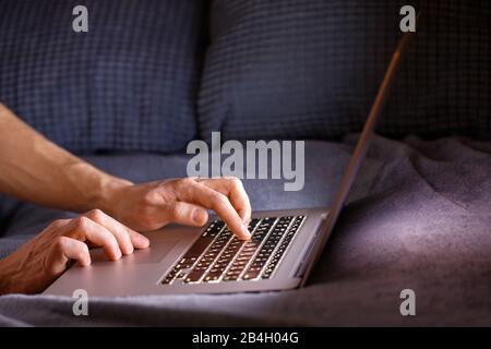 Nahaufnahme von Mann Hände Tippen auf der Laptop-Tastatur nachts drinnen, Kopierraum. Telearbeit, Heimarbeit, freiberufliches Konzept Stockfoto