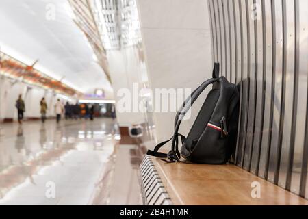 Vergessene schwarze Lederrucksack/Tasche oder Bombe zum Vergehen eines Terroranschlags liegt auf einem Sitz in der U-Bahn-Station, öffentlichen Verkehrsmitteln, verschwommener Passagier auf Bac Stockfoto