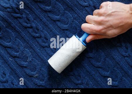 Man Hand mit einer klebrigen Walze zum Reinigen von Stoffen - Strickpullover aus Wolle vor Staub, Haaren, Flusen und Flusen, Draufsicht, Nahaufnahme. Stockfoto