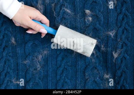 Frau Hand mit einer klebrigen Walze zum Reinigen von Stoffen - Strickpullover aus Wolle aus Staub, Haaren, Flusen und tierischem Flaum, Draufsicht, Nahaufnahme. Stockfoto