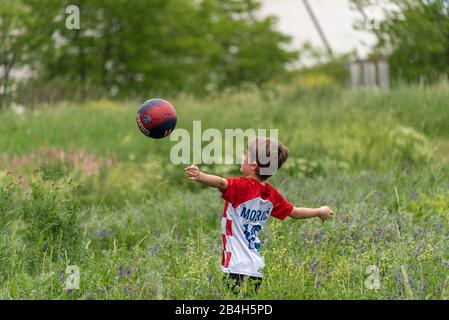 Ein acht Jahre alter Junge spielt im hohen Gras Fußball und trägt ein T-Shirt des kroatischen Fußballers Luka Modric Stockfoto