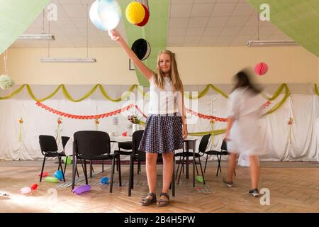 Ein Mädchen hält einen Ballon in der Luft, während andere Partygäste aufräumen oder bereits weg sind, Stockfoto