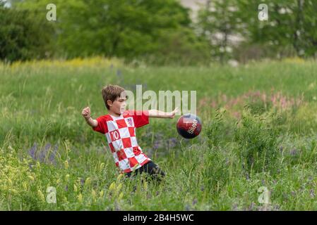 Ein kleiner Junge mit kroatischem Trikot spielt Fußball im hohen Gras, Stockfoto