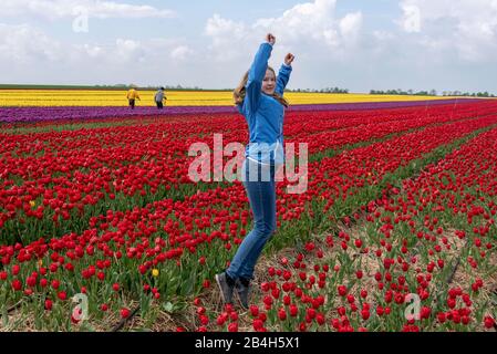 Ein zwölf Jahre altes Mädchen zieht sich die Arme und springt glücklich in ein Tulpenfeld Stockfoto