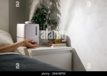 Schalten Sie den Aromaöldiffusor nachts am Nachttisch zu Hause ein, Dampf aus dem Luftbefeuchter. Ultraschalltechnologie, Erhöhung der Luftfeuchtigkeit Stockfoto