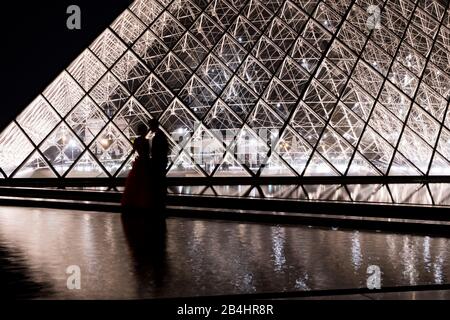 Ein Brautpaar nackt vor der beleuchteten Glaspyramide im Louvre spiegelt sich im Wasser, Paris, Frankreich, Europa Stockfoto