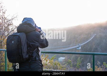 Deutschland, Sachsen-Anhalt, Oberharz, Tourist mit Rucksack, schaut durch Fernglas, Hängebrücke an der Rappbodetalsperre, Harz. Stockfoto