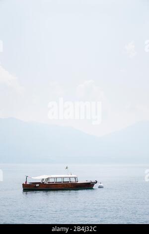 Europa, Italien, Piemont, Cannero Riviera. Vor dem Hafen am Lago Maggiore befindet sich ein kleines klassisches Ausflugsboot. Hinter dem sonnigen Morgennebel das andere Ufer. Stockfoto