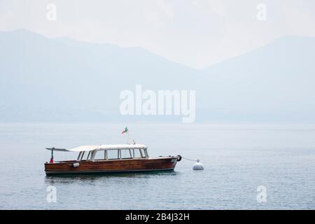 Europa, Italien, Piemont, Cannero Riviera. Vor dem Hafen am Lago Maggiore befindet sich ein kleines klassisches Ausflugsboot. Hinter dem sonnigen Morgennebel das andere Ufer. Stockfoto