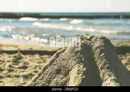 Nahaufnahme von Sandburg mit gläsernen Murmeln am Ostseestrand, das Meer im Hintergrund verwischt Stockfoto