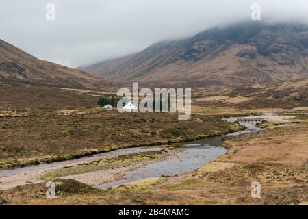 Großbritannien, Schottland, Highlands, Glencoe, White Cottage am Fluss mit Bergen im Nebel Stockfoto