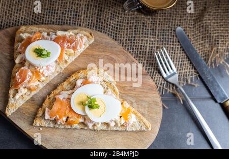 Ein köstlicher Räucherlachs, der aus Joghurt und Gewürzen auf einem ganzen Korn Brot Toast mit einer Tasse Kaffee auf der Seite zubereitet wird. Stockfoto