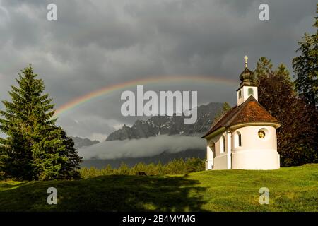 Die Kapelle Maria Königin am Lautersee bei Mittenwald mit Blick auf den Karwendel und einen großen Regenbogen Stockfoto