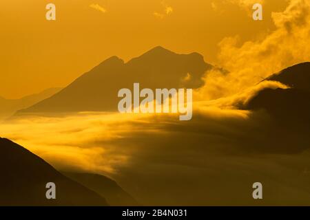 Hoher Nebel schwimmt im goldenen Abendlicht über das Plumsjoch im Karwendel, von den Rofan-Bergen aus gesehen. Stockfoto