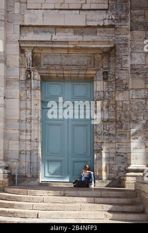 Junge Frau mit Handy sitzt auf dem Boden vor dem Portal der Kirche Saint-Pierre. Besançon ist eine Stadt in Ostfrankreich. Departement Doubs. Stockfoto