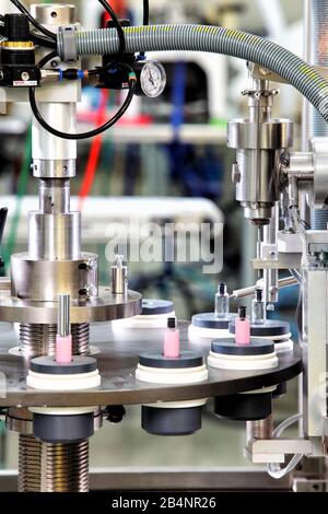 Ein Karussell mit leeren Fläschchen, die auf einer Füllmaschine für Fläschchen in einer Kosmetikfabrik gefüllt werden. Stockfoto