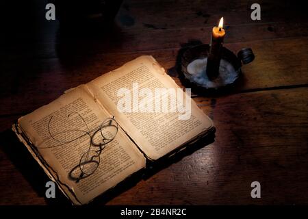 Ein Kerzenstock aus der antiken Kolonialzeit, der ein altes Delapidiertes Buch und Leseglas beleuchtet. Stockfoto