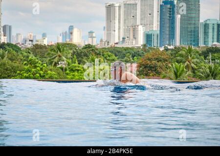 Ein Mann schwimmt einen Schmetterling in einem Pool auf dem Dach eines Luxushotels. Blick auf die Stadt Manila vom Pool des luxuriösen Fünf-Sterne-Discovery Primea Hot Stockfoto