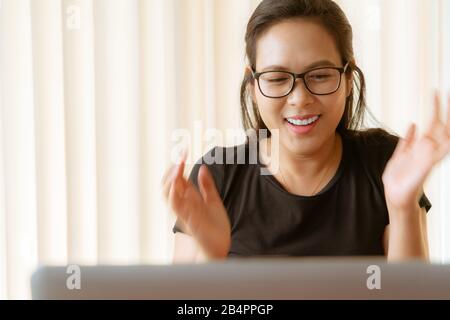 Glückliche Frau mit Laptop. Junge asiatische Frau, die zu Hause sitzt und am Laptop arbeitet Stockfoto