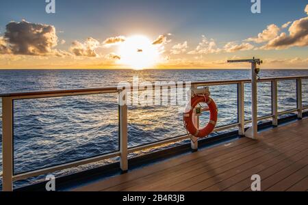 Sonnenuntergang im Kreuzfahrt-Urlaub. Sonne knapp über dem Horizont und Promenadendeck mit Geländer im Vorderteil. Stockfoto